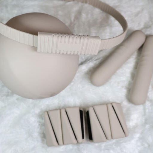 Beige exercise ball, resistance ring, weighted dumbbells and bangles on a white blanket