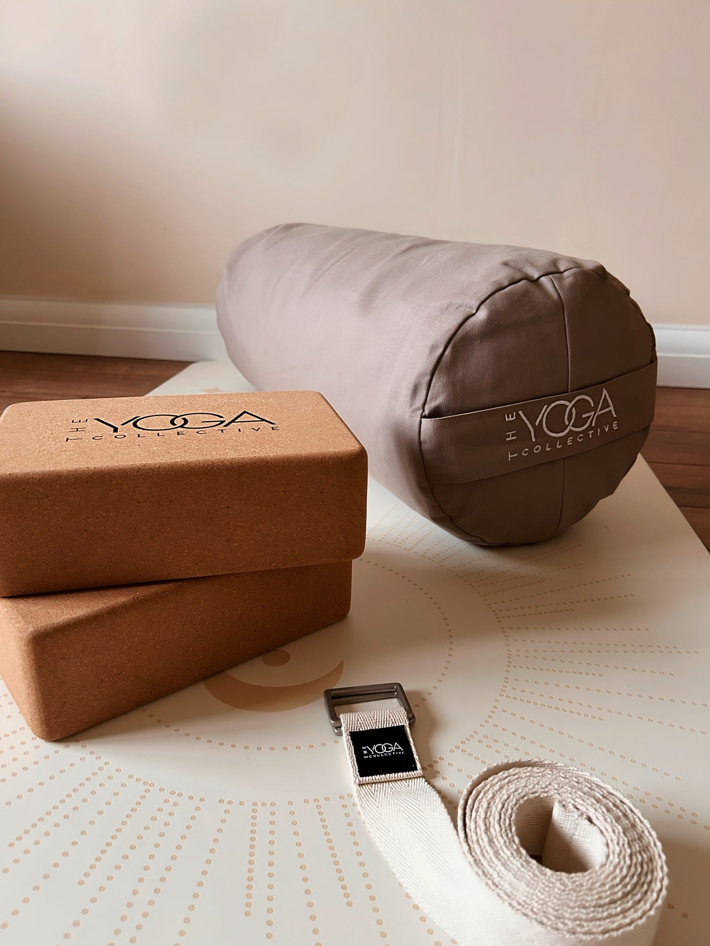 Yoga accessories including a brown yoga block, roller, and strap on a mat with 'The Yoga Shop' branding.